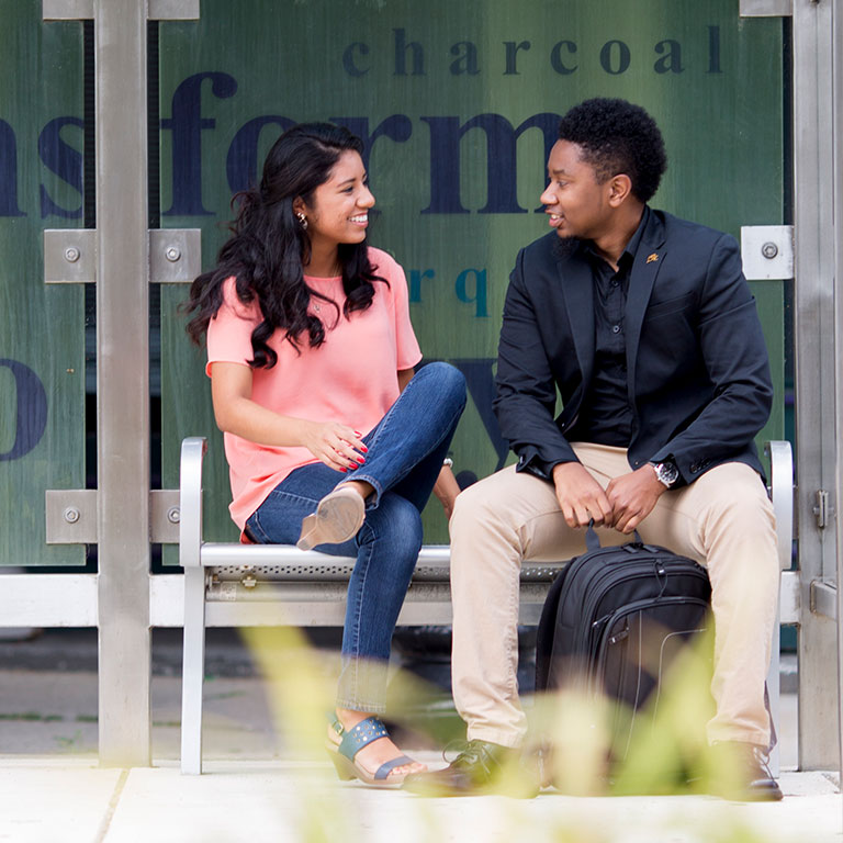 Two students engaging in conversation at a bus stop.